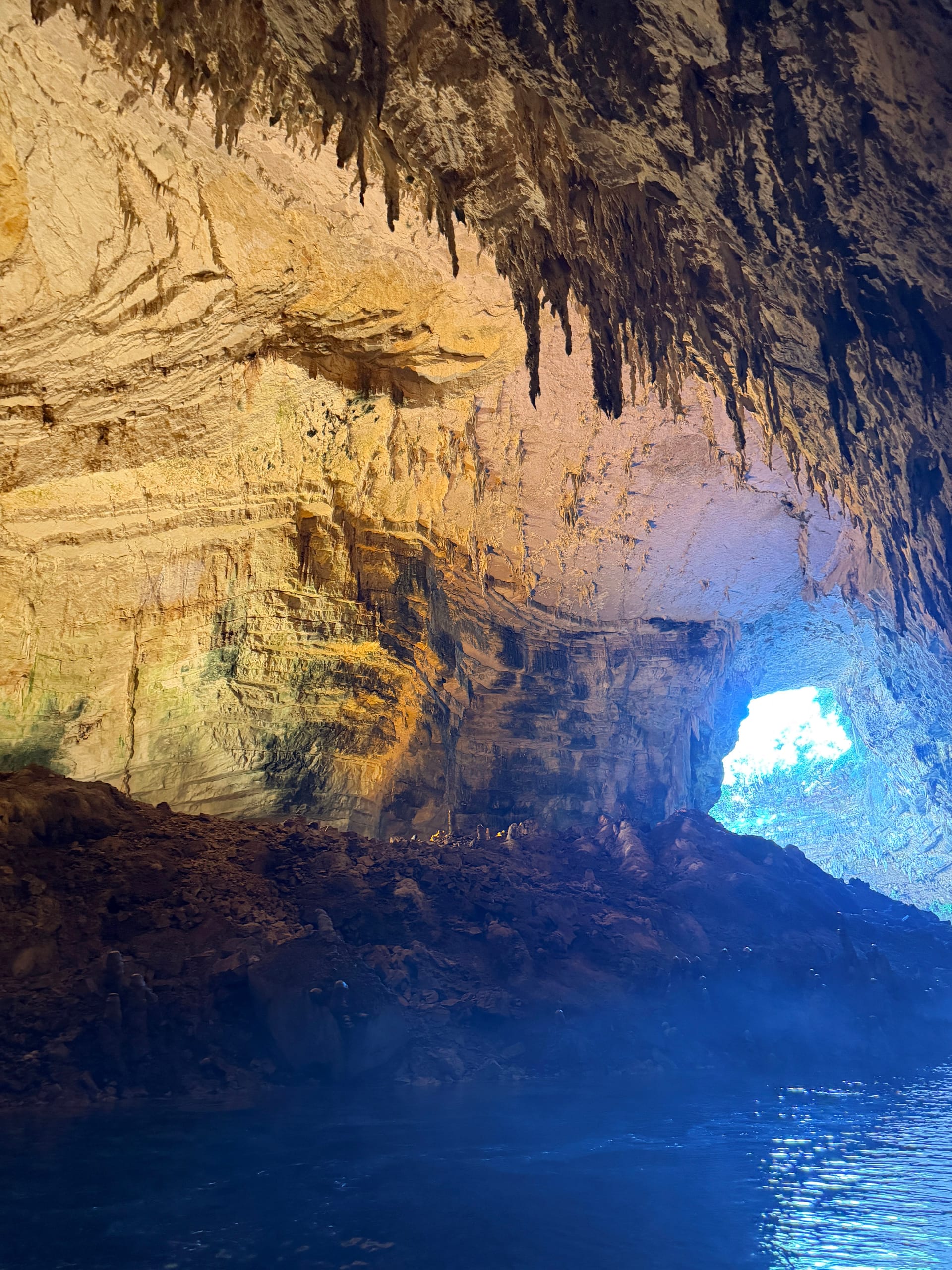 Inside Melissani cave — stalactites over the blue lake, daylight breaking through the collapsed roof