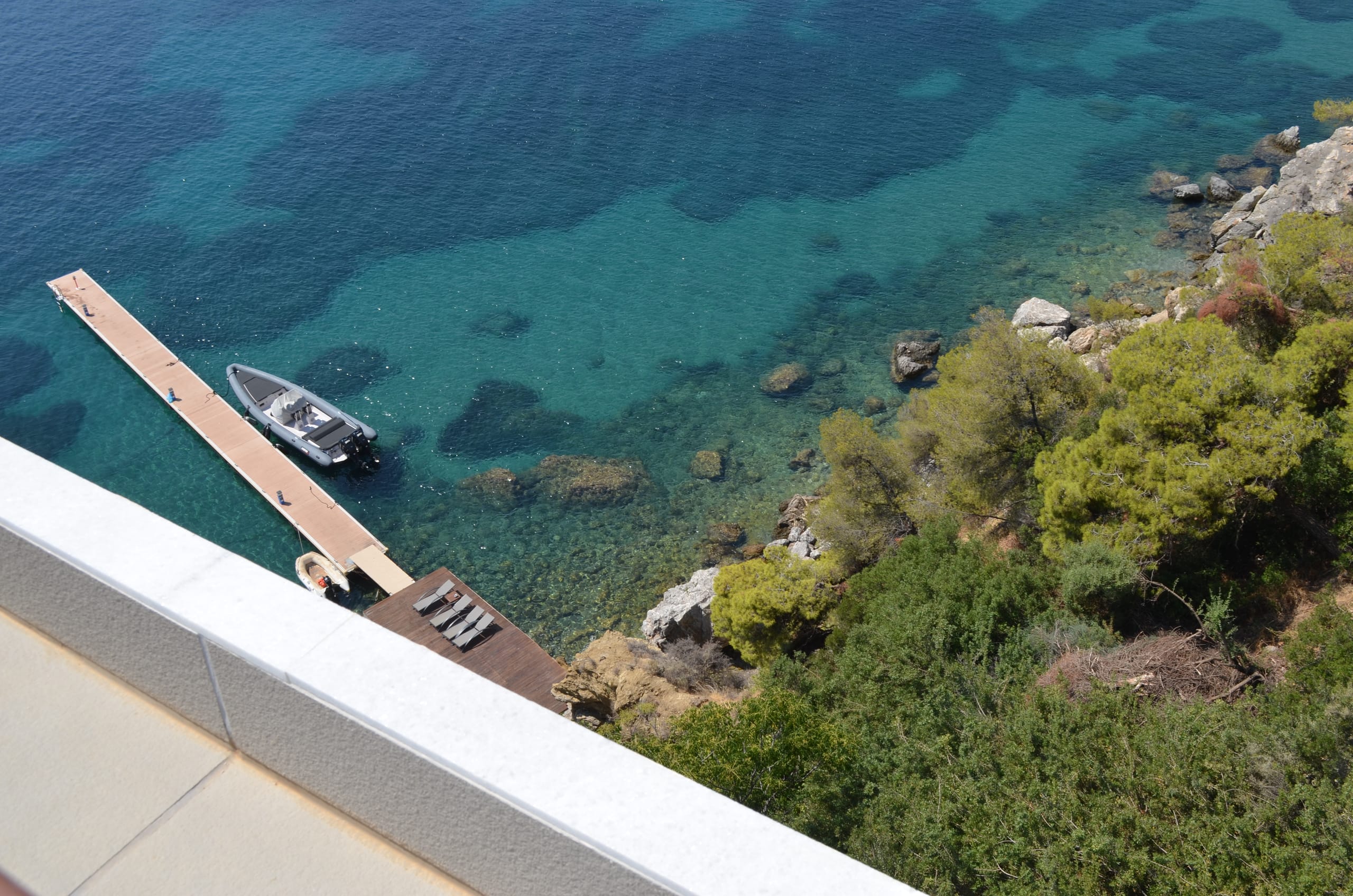 A jetty and moored boat over clear rock-bottomed water on Poros, pines meeting the shore