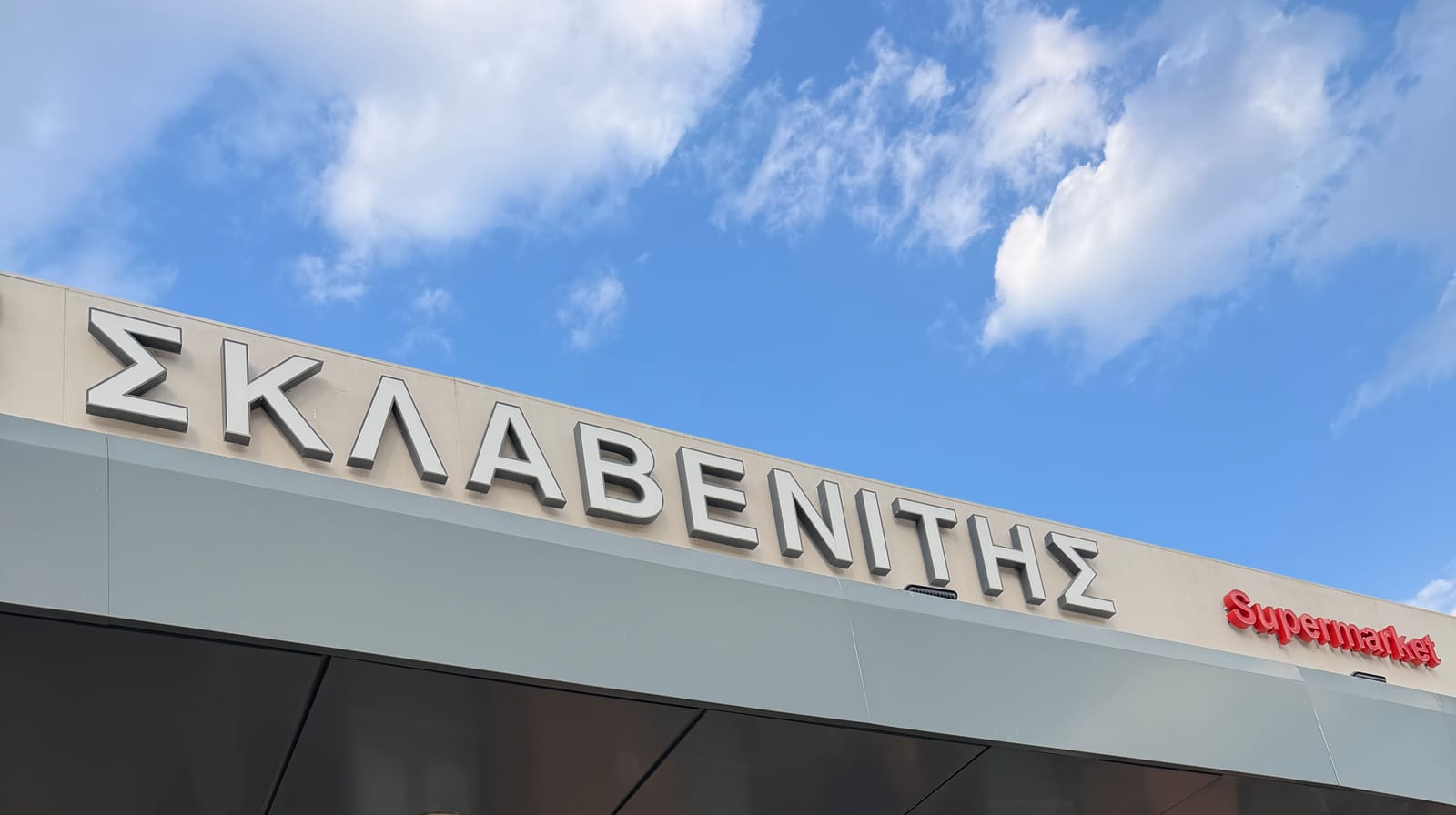 The fascia of a Sklavenitis supermarket against a blue sky, the chain name in large Greek capitals