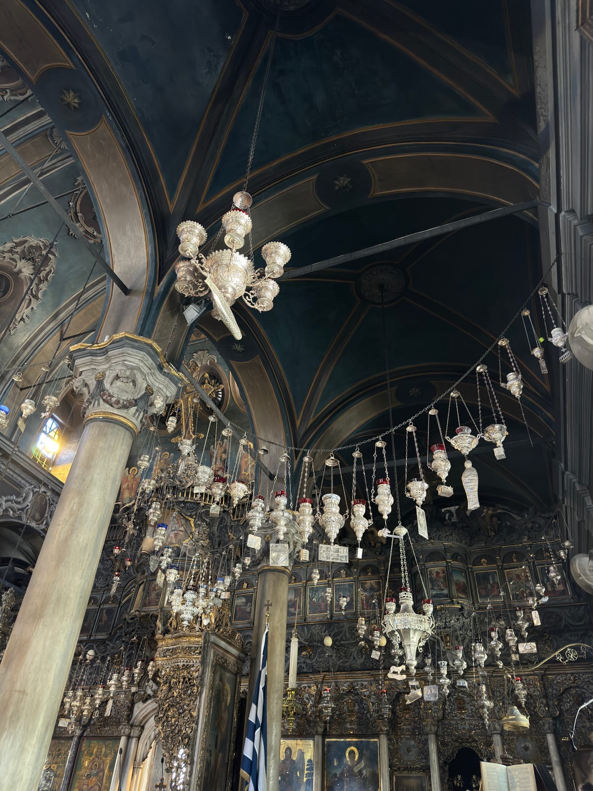 Silver votive lamps and hanging model ships beneath the painted vaulted ceiling of Panagia Evangelistria